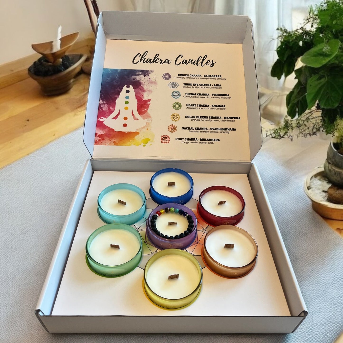 Set of seven Sheba Scents chakra candles in frosted glass jars, each with a unique color and label representing a each of the chakras, displayed in a calming, spiritual setting in a gift set box