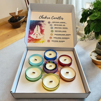 Set of seven Sheba Scents chakra candles in frosted glass jars, each with a unique color and label representing a each of the chakras, displayed in a calming, spiritual setting in a gift set box
